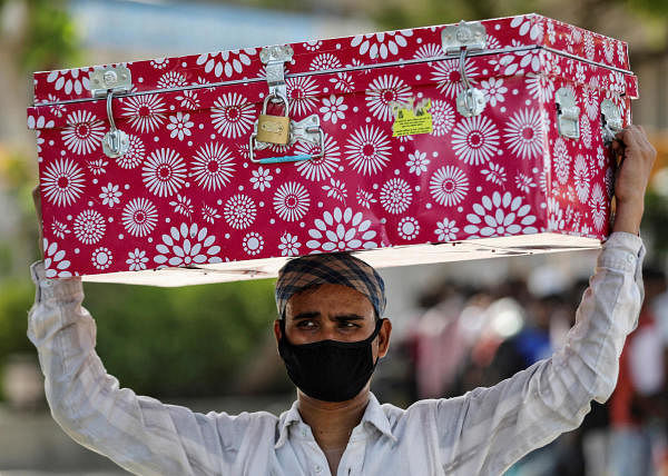 A migrant worker carries a luggage trunk on his head as he waits for transport to reach a railway station to board a train to his home state of Bihar, during an extended lockdown to slow the spreading of the coronavirus disease (COVID-19), in Ahmedabad, India, May 23, 2020. (Credit: Reuters Photo)