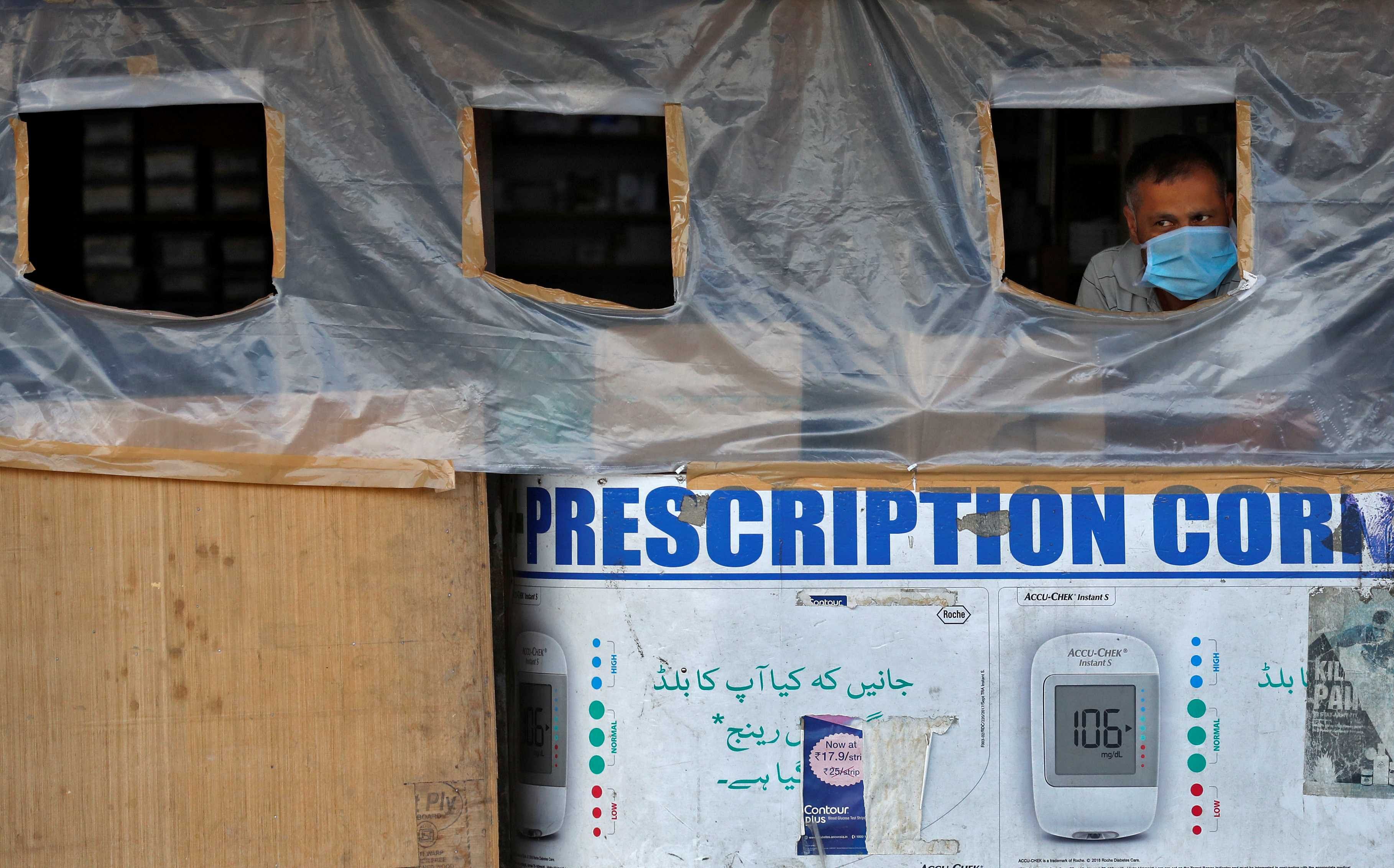 A man wearing a protective mask looks out from a pharmacy shop covered with a plastic sheet to maintain social distance during a lockdown to slow the spread of the coronavirus disease (COVID-19), in Srinagar. (Credit: Reuters photo)