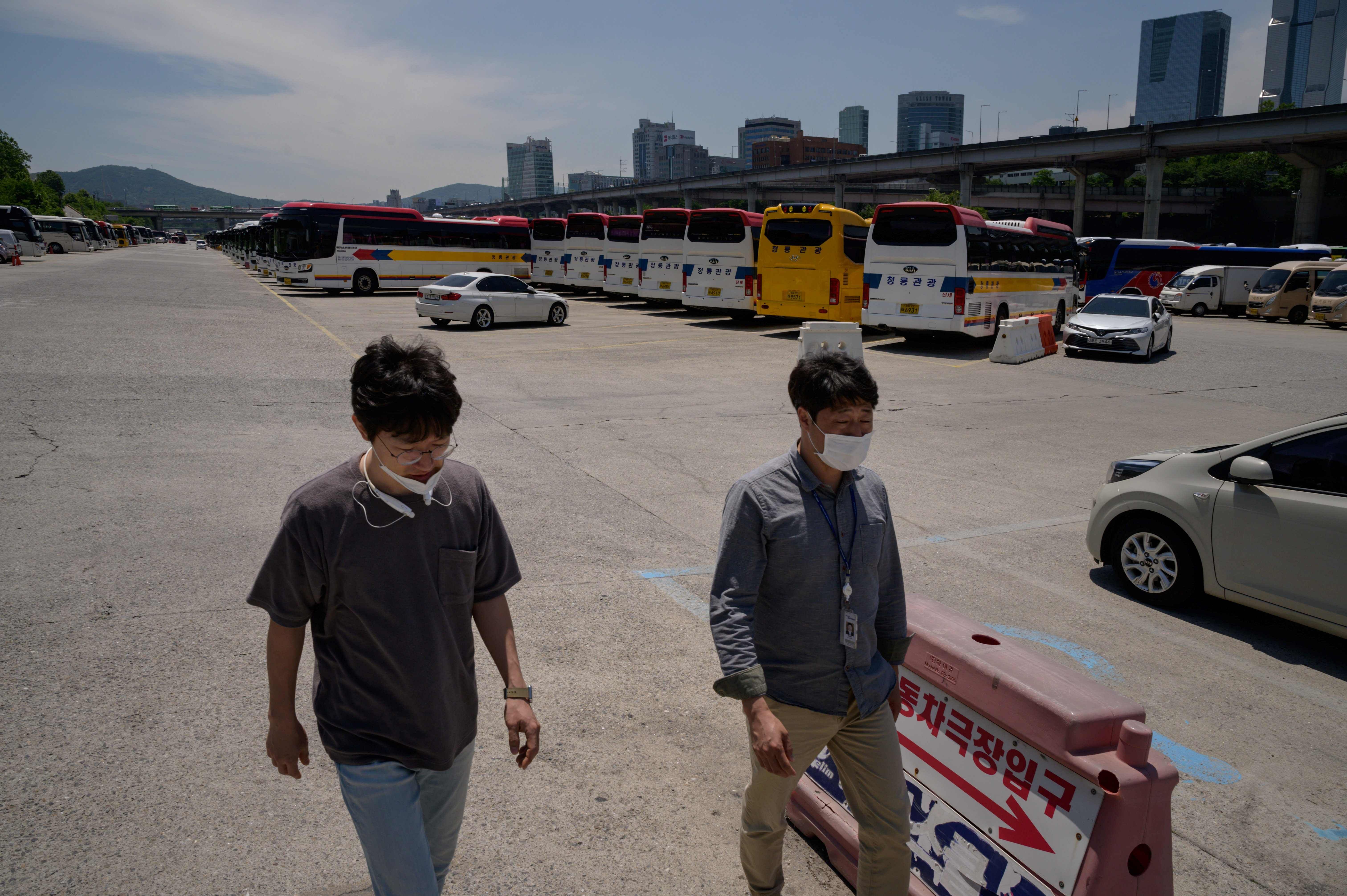 Two men wearing face masks walk before tour busses stored in a parking lot in Seoul amid a downturn in tourism due to the covid-19 novel coronavirus pandemic. (AFP Photo)