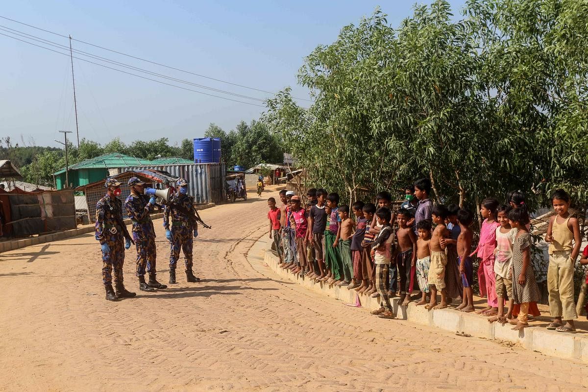 In this file photo taken on May 15, 2020 Security personnel (L) use a loudspeaker to raise awareness about the COVID-19 coronavirus in a Rohingya refugee camp in Ukhia. AFP