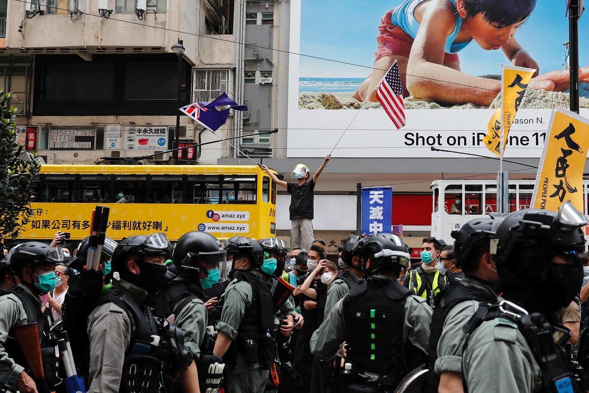 An anti-government protester waves the U.S. and the British colonial Hong Kong flags as riot police walk past during a march against Beijing's plans to impose national security legislation in Hong Kong, China May 24, 2020. (REUTERS Photo)