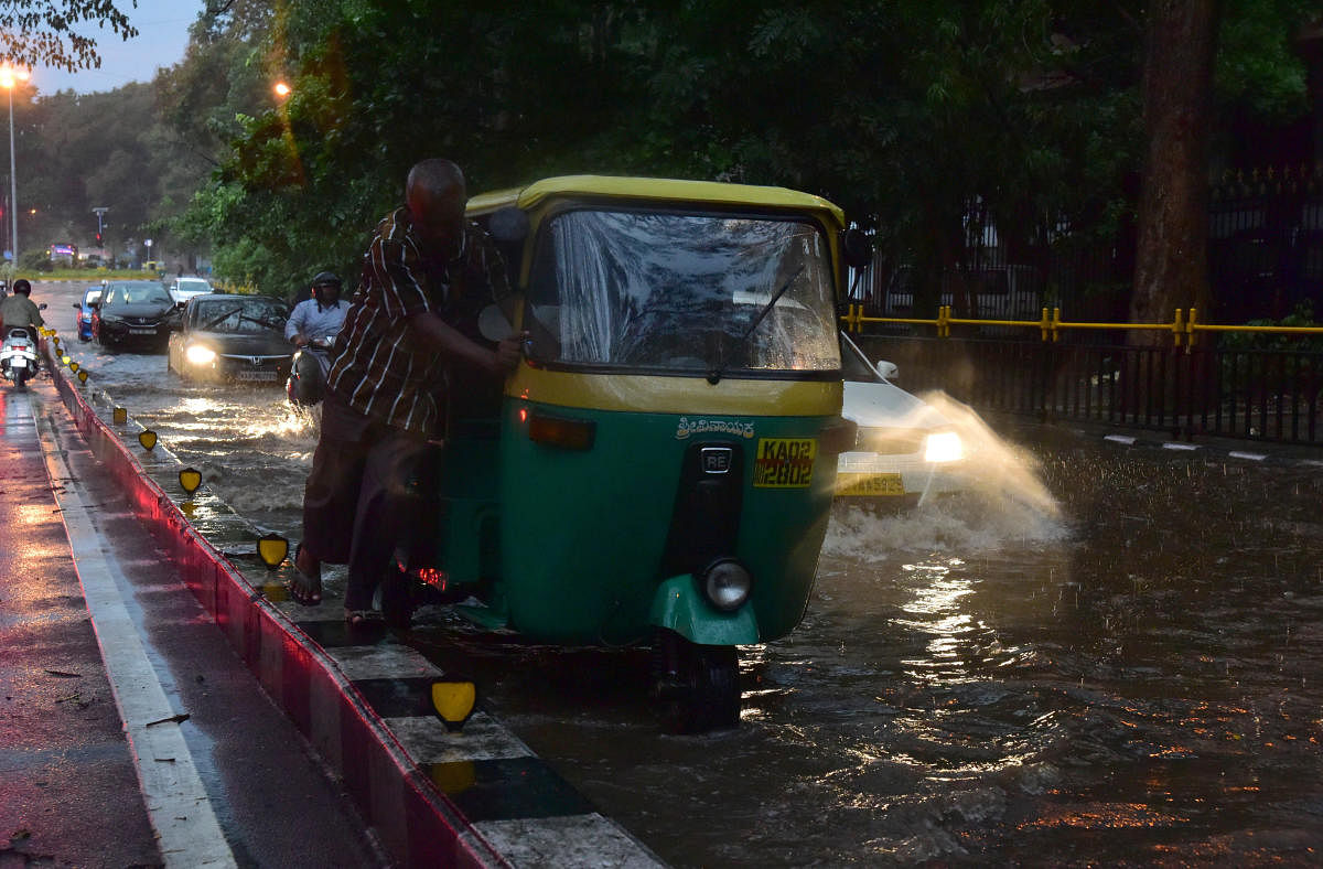 An autorickshaw driver struggles to push his vehicle along a waterlogged Ambedkar Veedhi near KR Circle on Friday. DH photo/IRSHAD MAHAMMAD