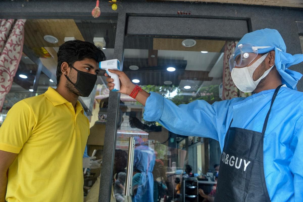 An employee wearing a protective gear (R) checks the body temperature of a customer at the entrance of a men beauty parlour after the government eased a nationwide lockdown as a preventive measure against the COVID-19 coronavirus, in Siliguri. (AFP Photo)