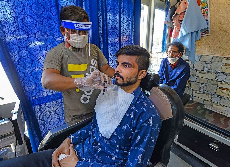  A barber, wearing a face-shield amid concerns over COVID-19 outbreak, attends a customer at his shop. (PTI Photo)