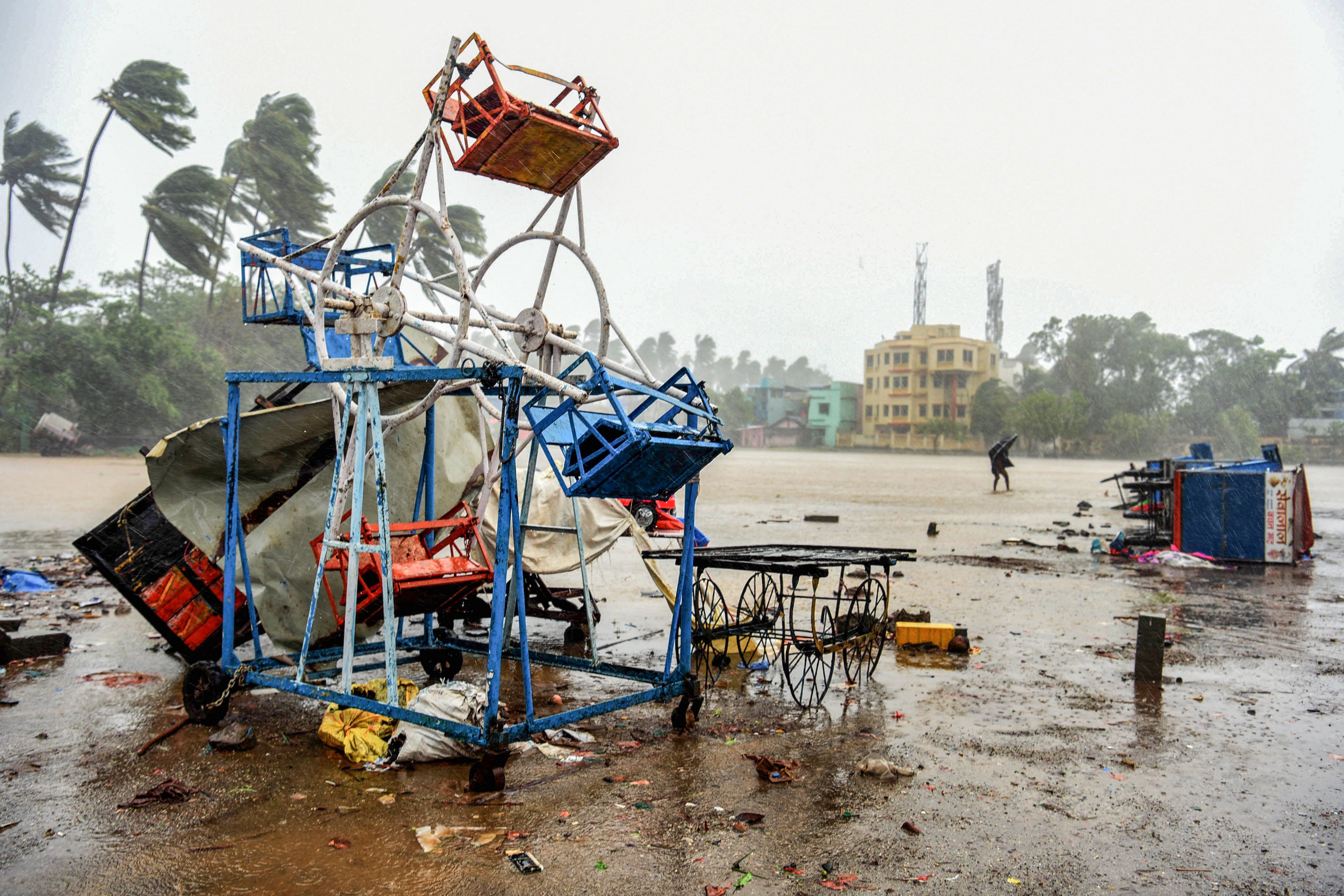 A man holding an umbrella walks past a small damaged ferris wheel and shacks at the beach in Alibag town of Raigad district. (AFP Photo)
