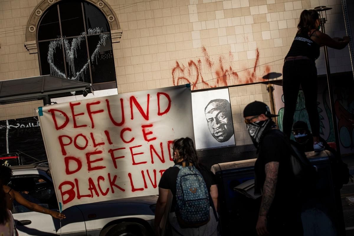 Demonstrators hang a sign next to a mural (back R) of George Floyd, who died in Minneapolis on May 25 whilst in police custody, during a "Sit Out the Curfew" protest in downtown Oakland, California. AFP
