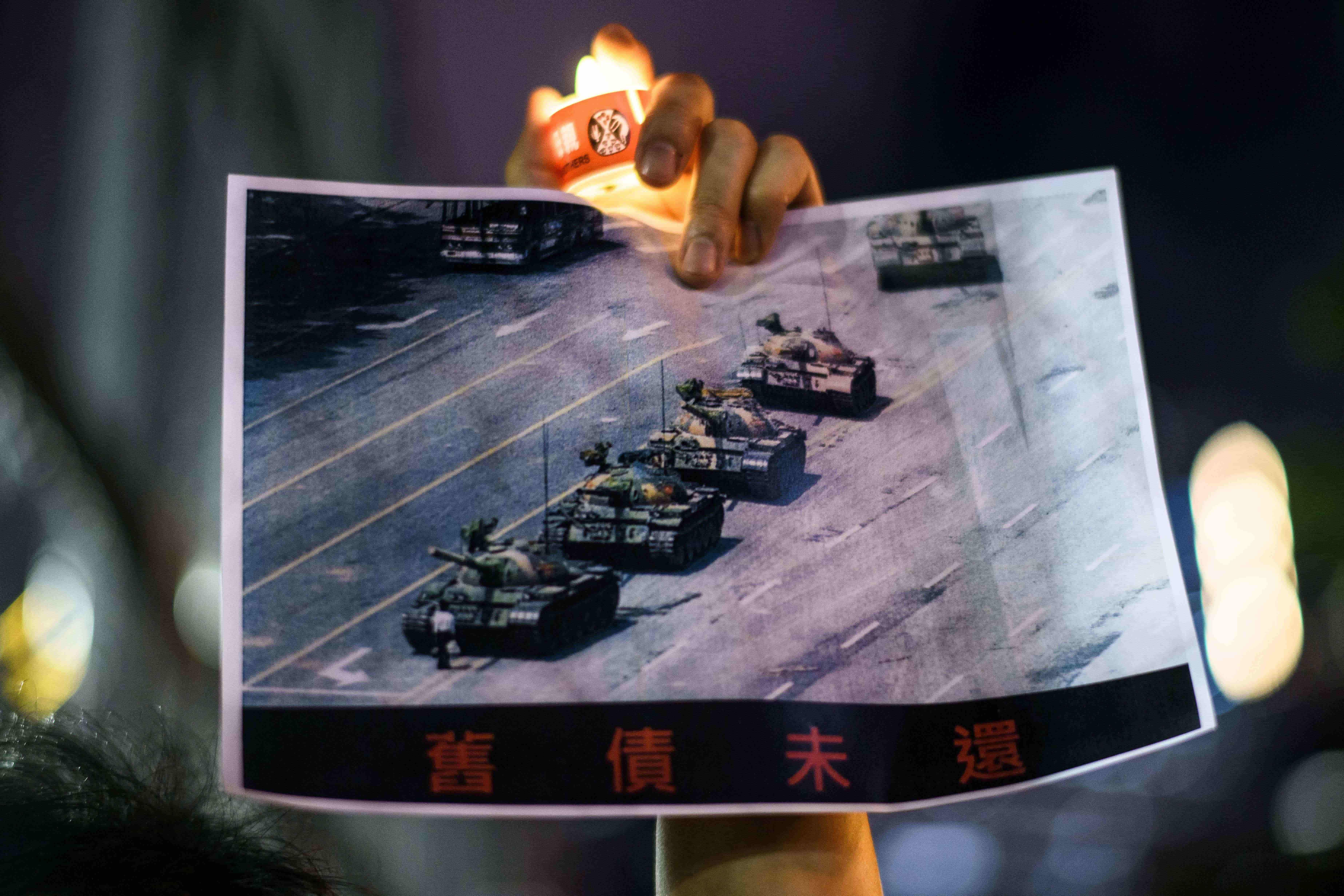 A man holds a poster of the famous 'Tank Man' standing in front of Chinese military tanks at Tiananmen Square in Beijing on June 5, 1989. (Credit: AFP Photo)