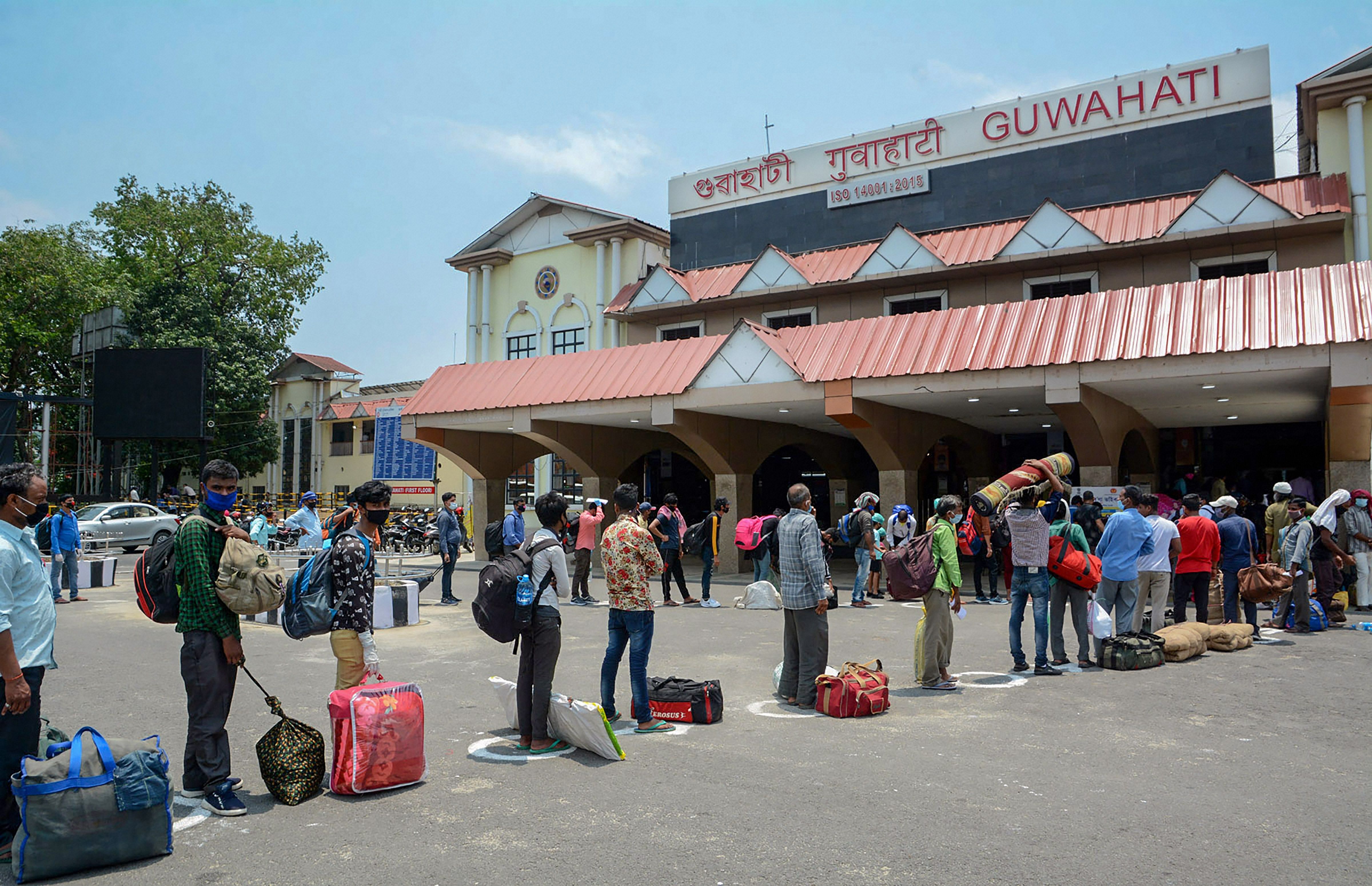 Passengers along with their luggage stand in a queue outside Guwahati Railway station to board a train, during the ongoing COVID-19 lockdown, in Guwahati. (PTI Photo)