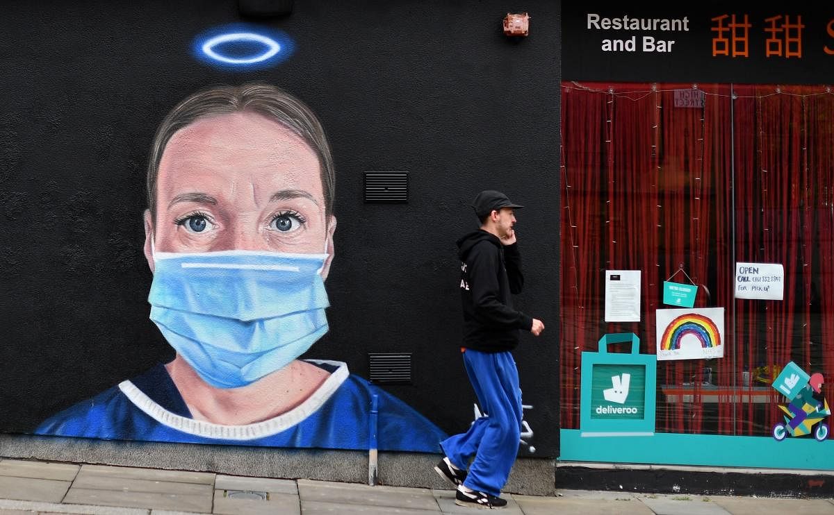 A pedestrian walks past street art graffiti, by the artist @akse_p19, depicting a nurse in scrubs and a face mask, but with an Angel's halo above her head, in Manchester, northern England, on June 3, 2020. Credit/AFP Photo