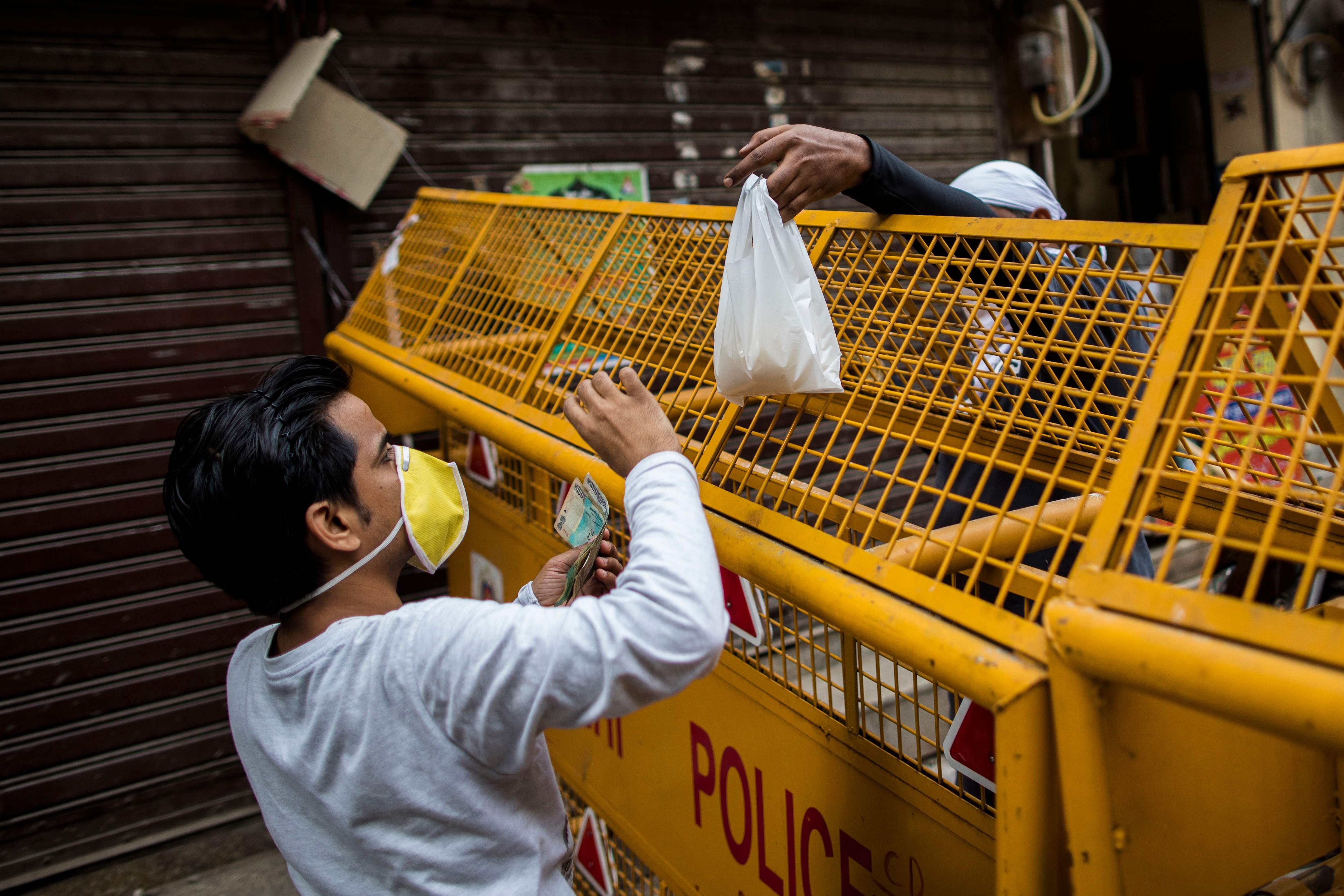 A resident (L) buys items from a vendor across a barrier in a containment zone due to COVID-19 cases in the neighbourhood, after the government eased a nationwide lockdown imposed as a preventive measure against the COVID-19 coronavirus, in the old quarters of New Delhi on June 5, 2020. (Photo by AFP)