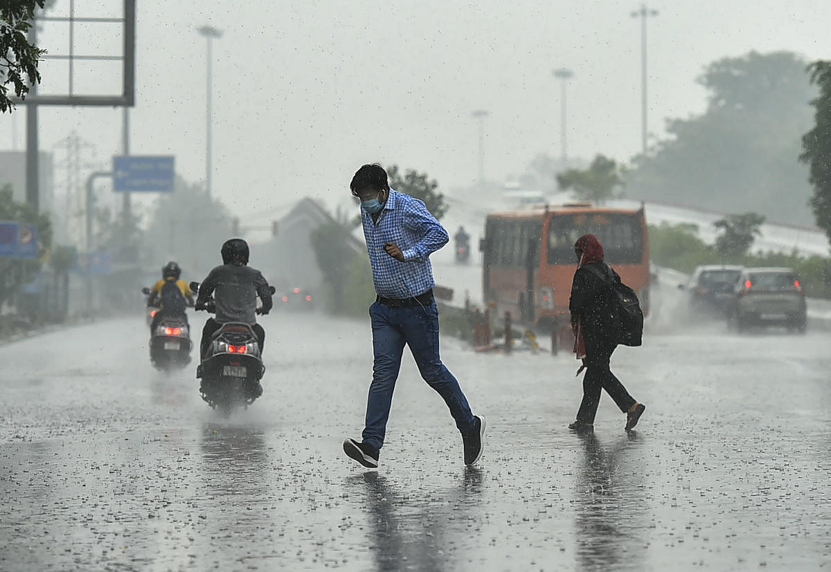 People run for cover as it rains in New Delhi. PTI