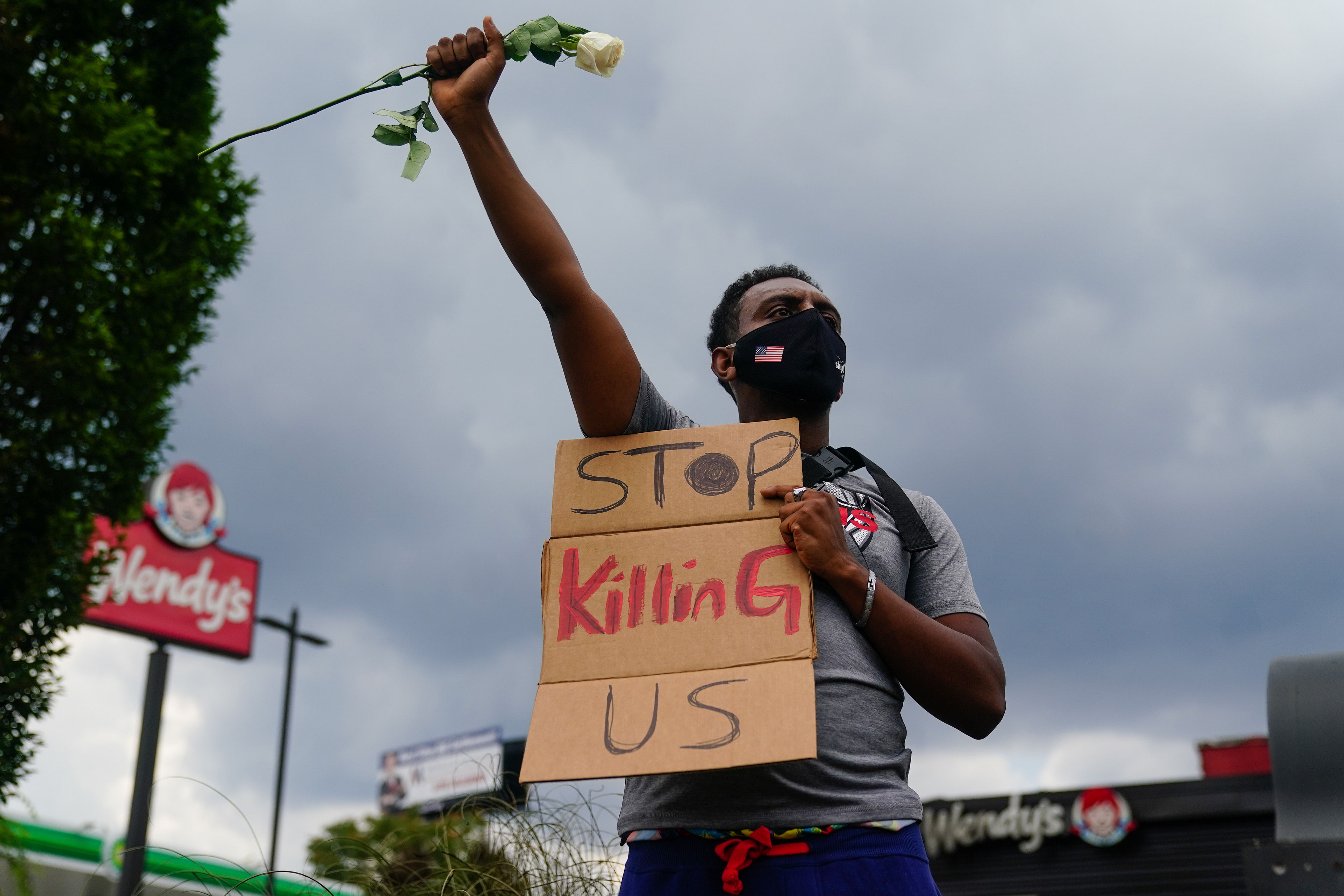 A man holds a sign and a white rose in his fist while facing traffic outside a burned Wendy’s restaurant on the second day following the police shooting death of Rayshard Brooks in the restaurant parking lot June 14, 2020, in Atlanta, Georgia. - The fatal shooting of a black man by a white police officer, this time in Atlanta, Georgia, poured more fuel June 14, 2020 on a raging US debate over racism after another round of street protests and the resignation of the city's police chief. A Wendy's restaurant where 27-year-old Rayshard Brooks was killed was set on fire June 13, 2020 and hundreds of people marched to protest the killing. (Photo by AFP)