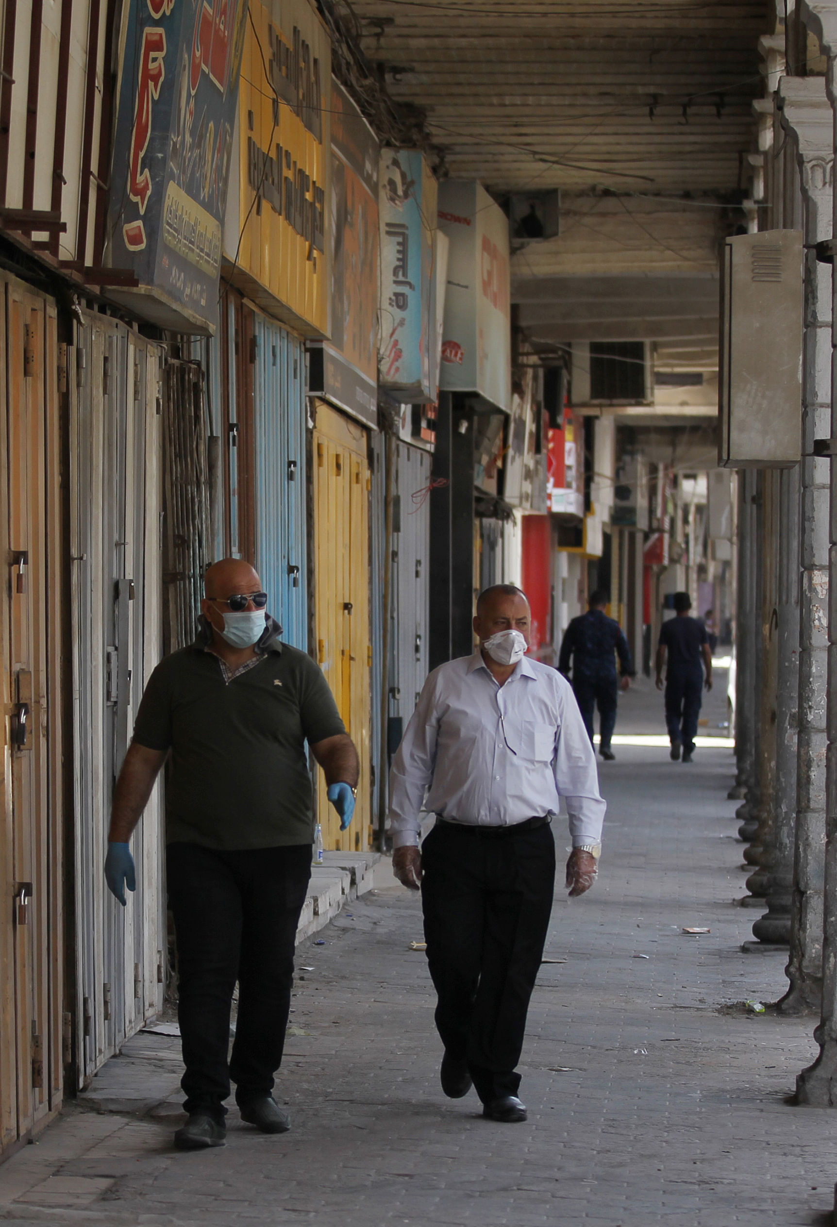 Iraqi men wearing protective masks walk through an empty commercial street. Credits: AFP Photo