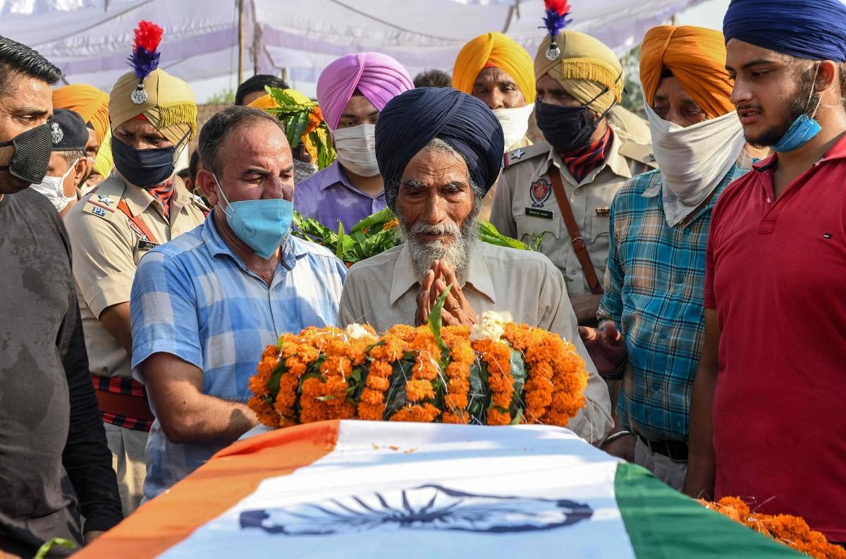 Jagir Singh (C) lays wreaths of flowers on the coffin of his son and soldier Satnam Singh who was was killed in a recent clash with Chinese forces in the Galwan valley area, during the cremation ceremony at Bhojraj village near Gurdaspur on June 18, 2020. Credit/AFP Photo
