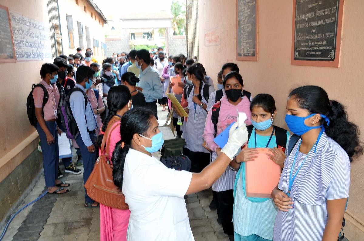 A staffer checks the temperature of the students at the Government PU College for Girls at Basavanahalli in Chikkamagaluru. DH Photo