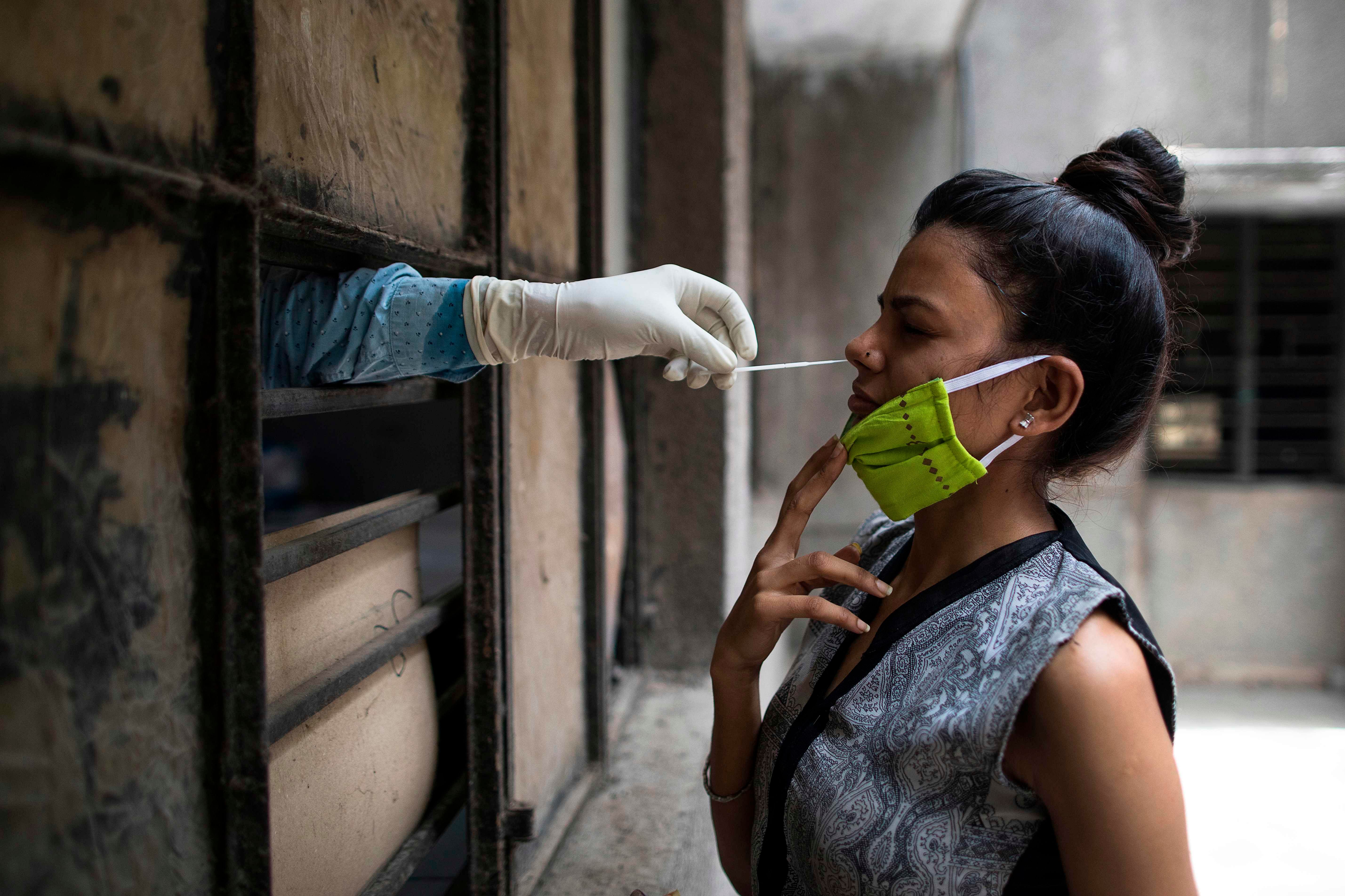 A health official (L) collects a swab sample from a woman to test for the COVID-19 coronavirus at a temporary free testing facility set up in a school in New Delhi. Credit: AFP