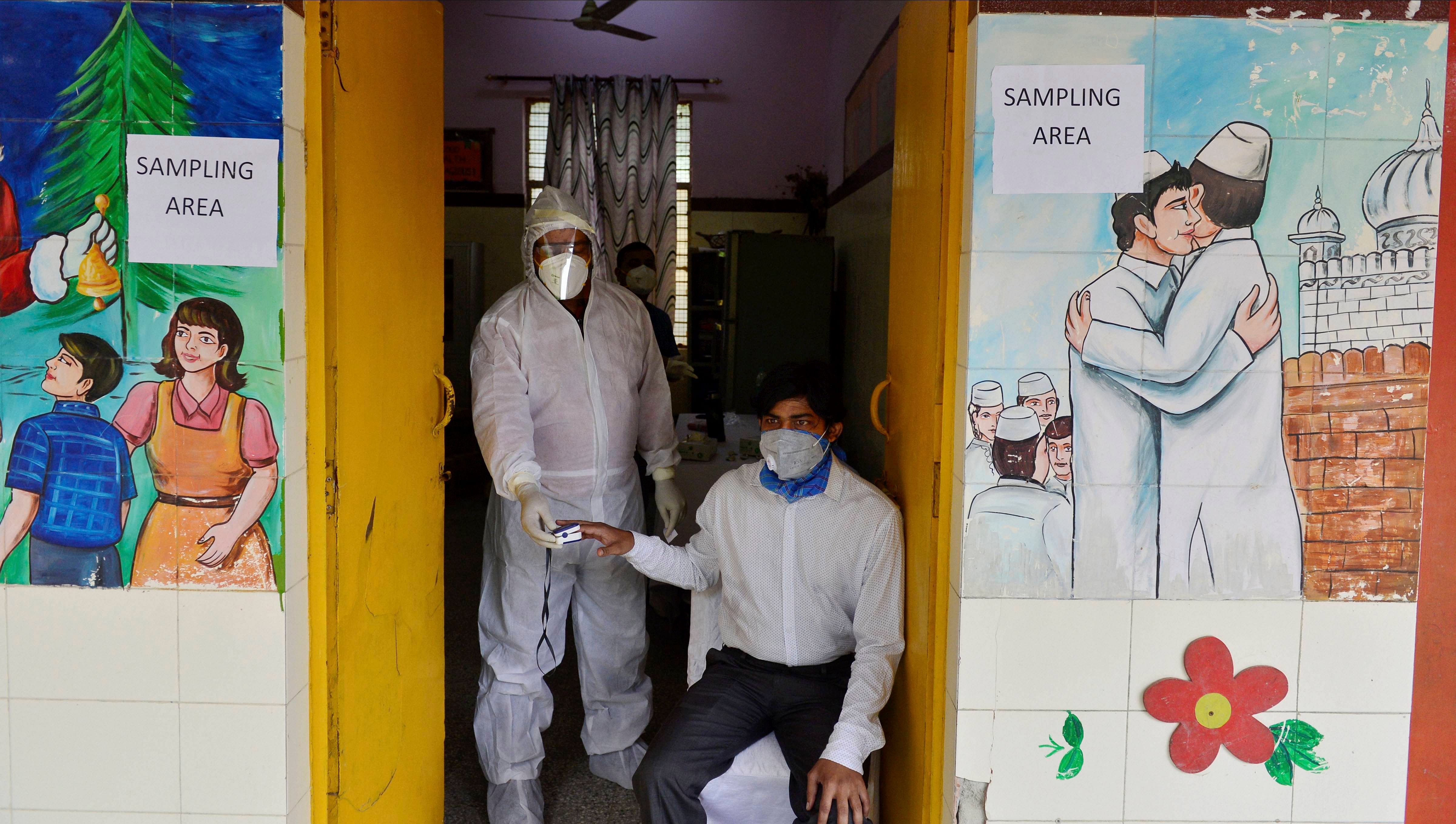 A health worker wearing a protective suit checks temperature of a man before taking his swab sample for COVID-19 test, in New Delhi. Credit: PTI Photo