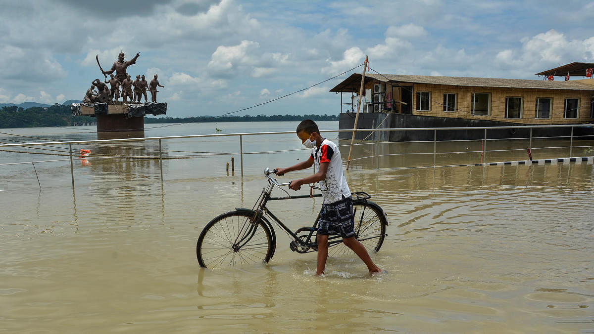 A boy walks with his cycle on a flooded road at the bank of Brahmaputra River, flowing above the danger mark, in Guwahati. Credit: PTI