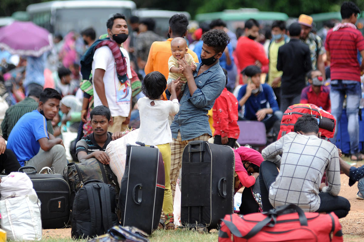 Women stand in a queue to get a bottle of water and a banana as hundreds of migrants and students from Assam arrive at Palace Grounds in Bengaluru after receiving a message about the Shramik train to Assam. However, officials delayed the process due to la