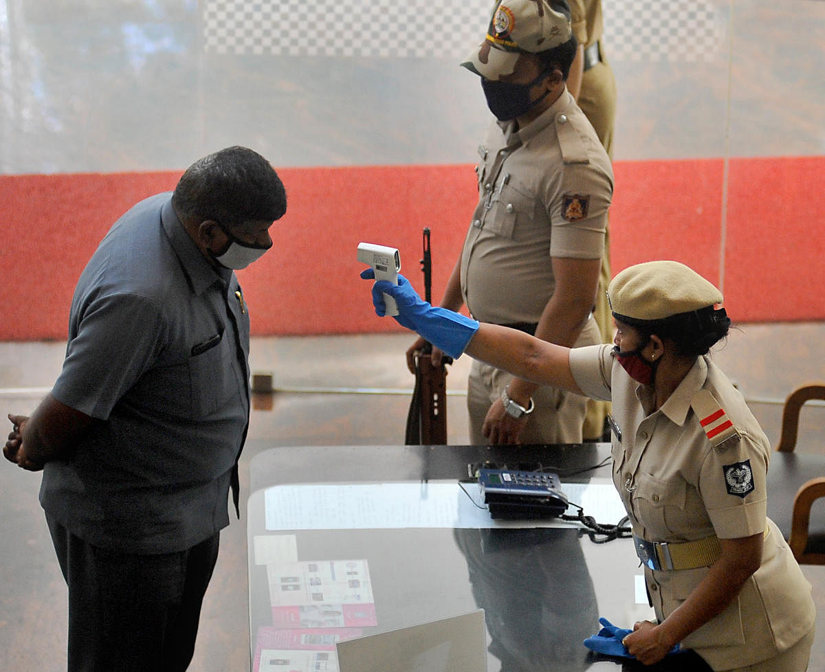 Police staff check body temperatures of visitors at city police commissioner office, Bengaluru on Wednesday. DH Photo/Pushkar V