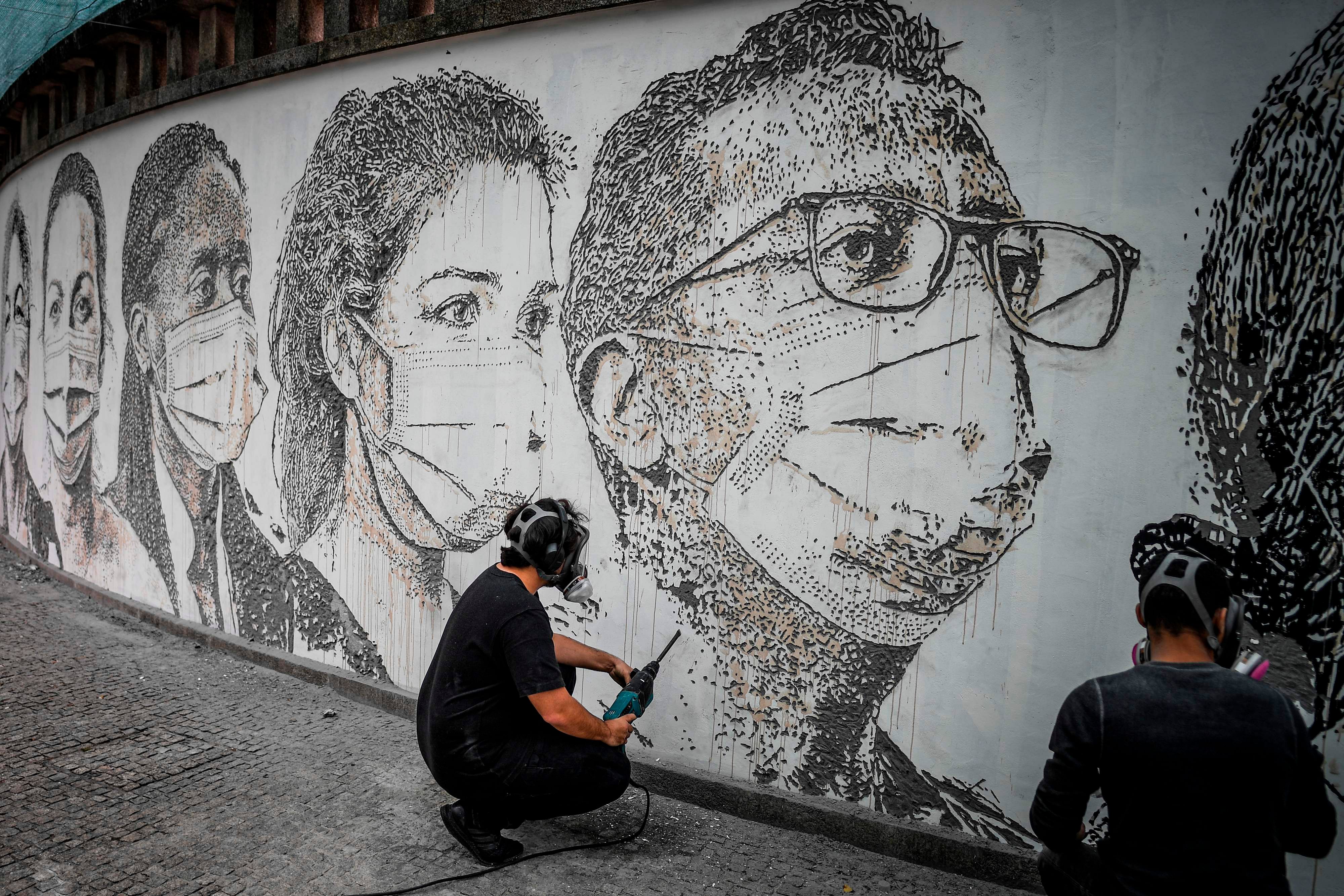 Portuguese artist Alexandre Farto aka Vhils works in his mural depicting healthcare workers' faces carved on a wall of Sao Joao Hospital in Porto on June 17, 2020. - Vhils unveiled on June 19, 2020 this carving-graffiti artwork at the Sao Joao hospital that pays tribute to the health professionals who were at the frontline fighting the novel coronavirus outbreak. (Photo by AFP)