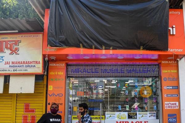 People stand outside a shop selling mobile phones from Chinese electronics company Xiaomi of which the front name is covered with a tarp, as calls for a boycott of Chinese goods gather pace following a border clash that killed 20 Indian soldiers, in Mumbai on June 25, 2020. Credit: AFP Photo