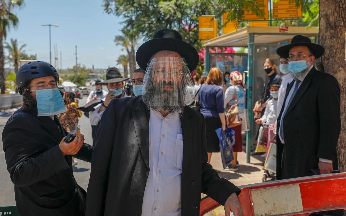 Ultra-Orthodox Jewish men, wearing protective masks, stand across a police checkpoint in Elad city in central Israel on June 24, 2020, as the government imposed a partial lockdown on several neighbourhoods following a recent increase in coronavirus cases. Credit/AFP Photo