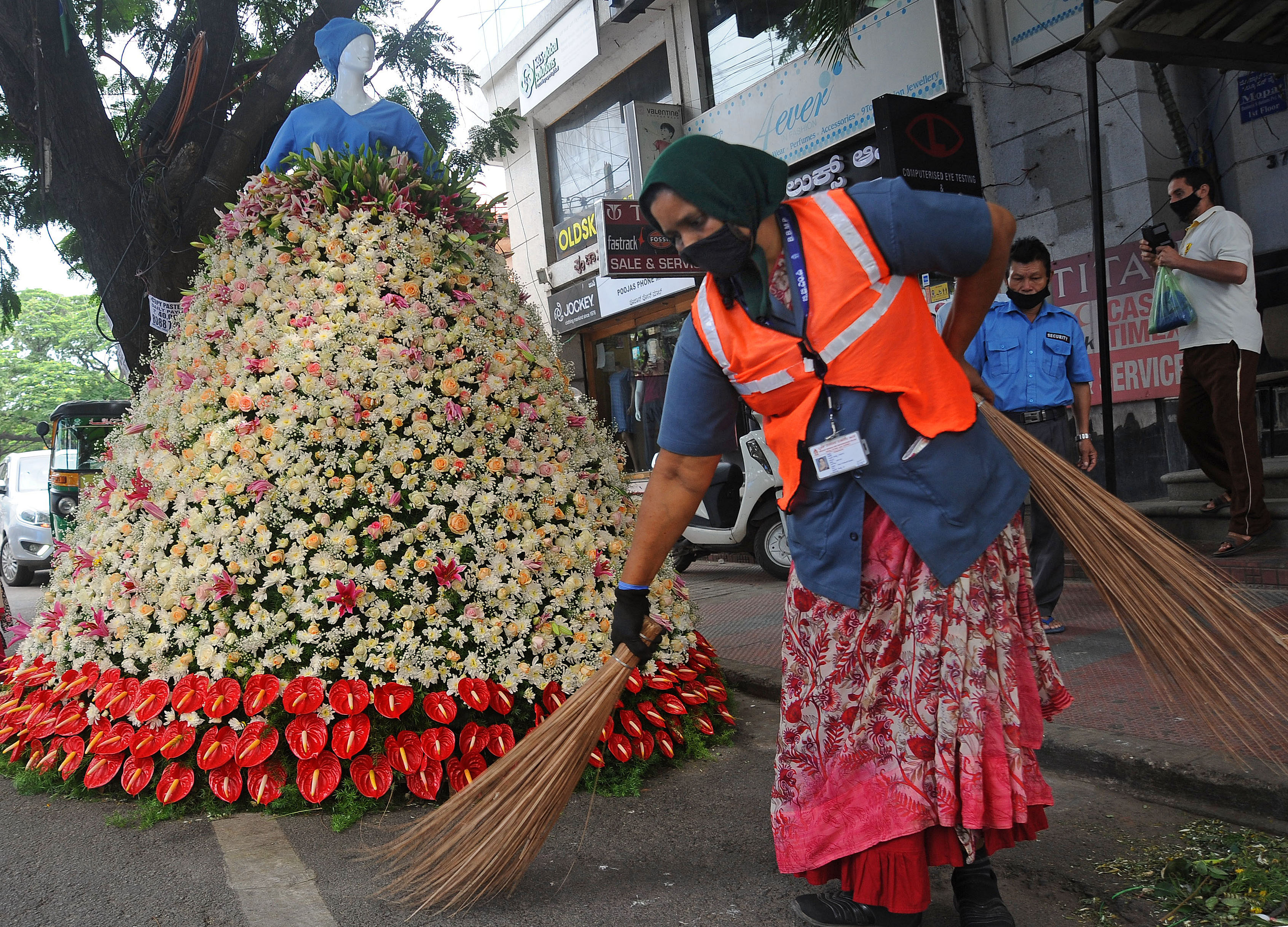 A pourakarmika sweeps in front of a floral tribute to coronavirus warriors at Mosque Road, Bengaluru. Credits: DH Photo
