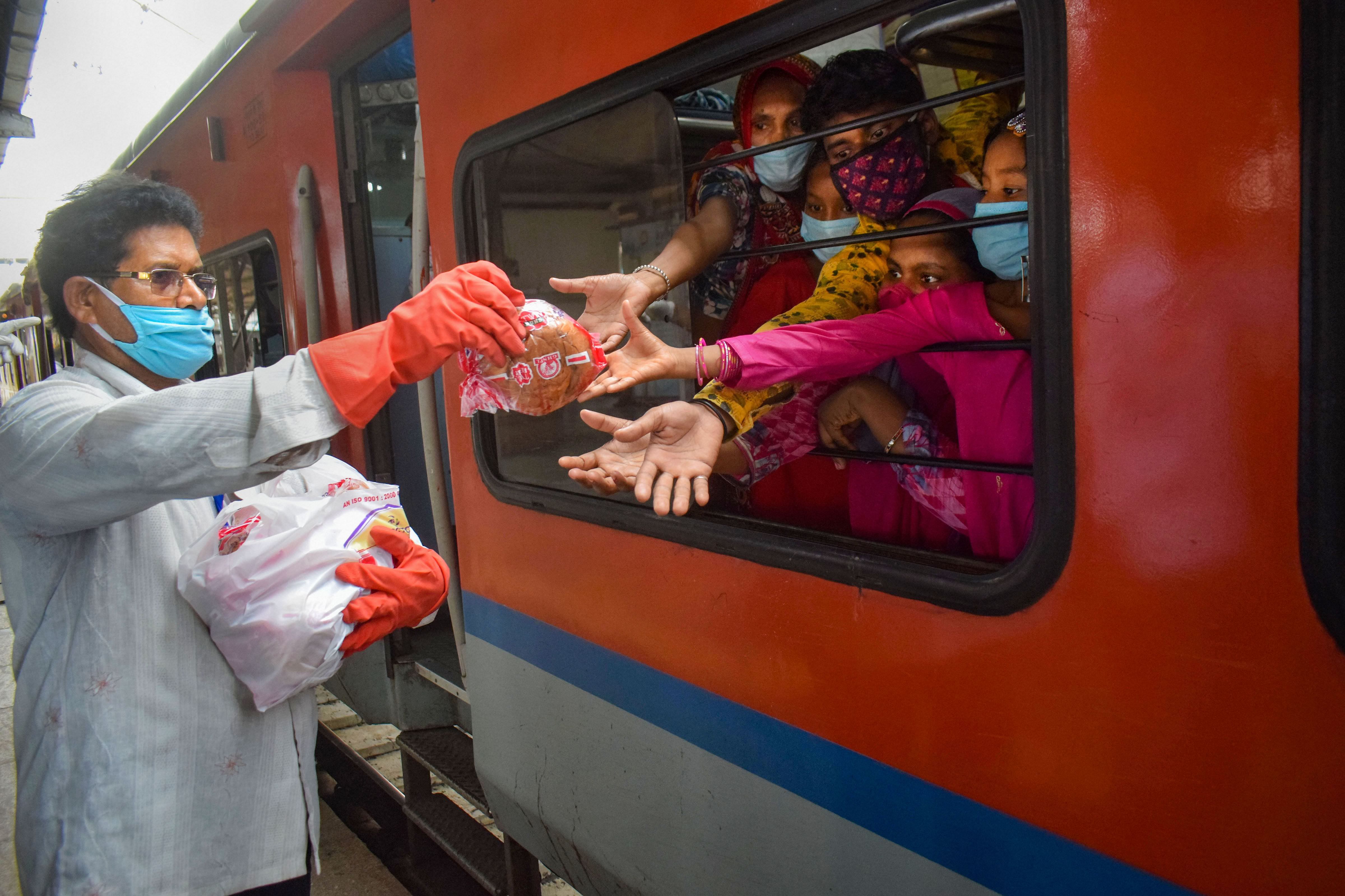  A railway staff member distributes food packets among migrants sitting in Shramik Special train. Credits: PTI Photo