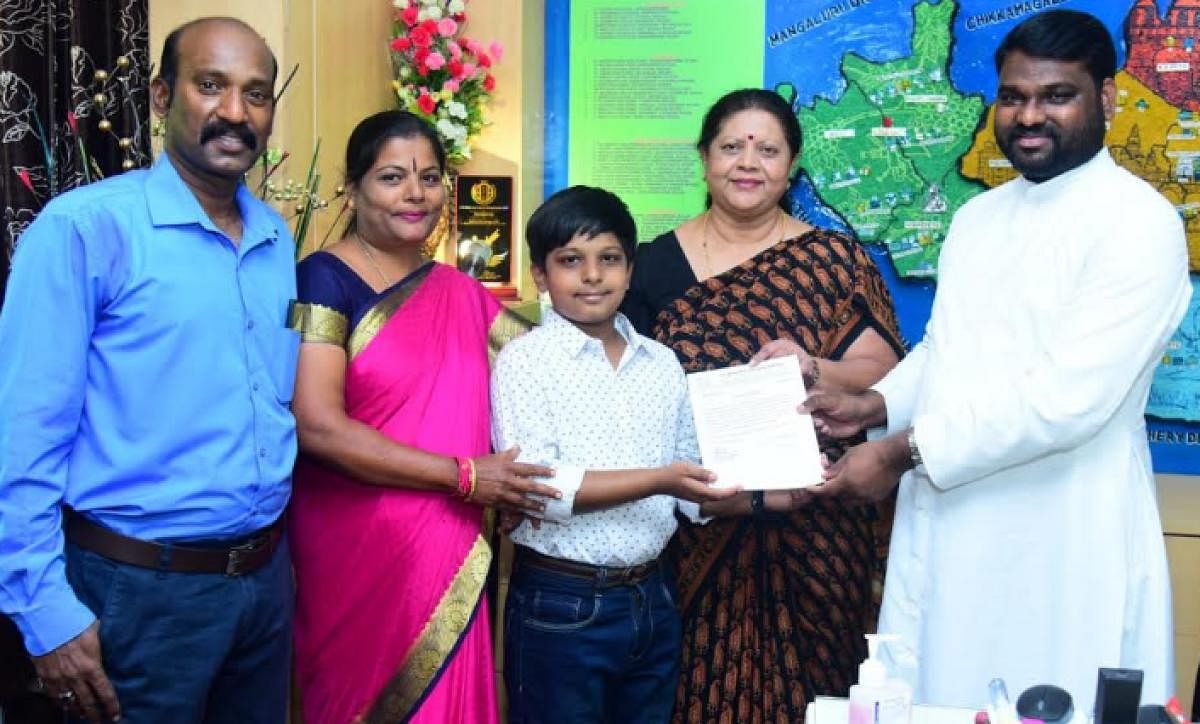 Mysore Diocesan Educational Society (MDES) secretary Vijay Kumar issues a certificate of appreciation to P Praneel in Mysuru. Praneel's father Premkumar P Wellington and mother Vijayalakshmi Manapura are seen.