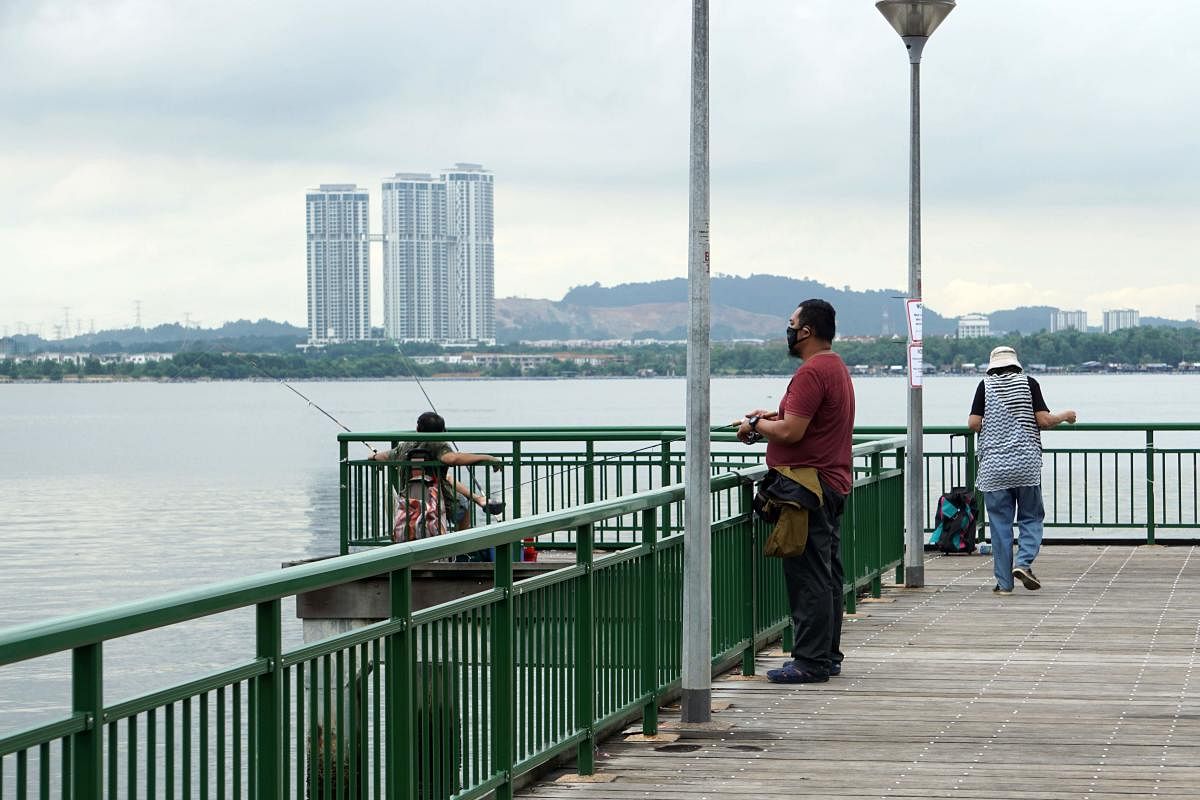 People fish from a jetty at a seafront in Singapore across Malaysia's southern state of Johor, seen in the background. AFP