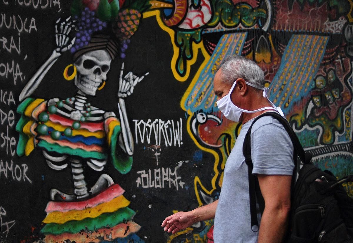 A man wearing a facemask walks past a mural in Rio de Janeiro, Brazil on July 1, 2020. Credit/AFP Photo
