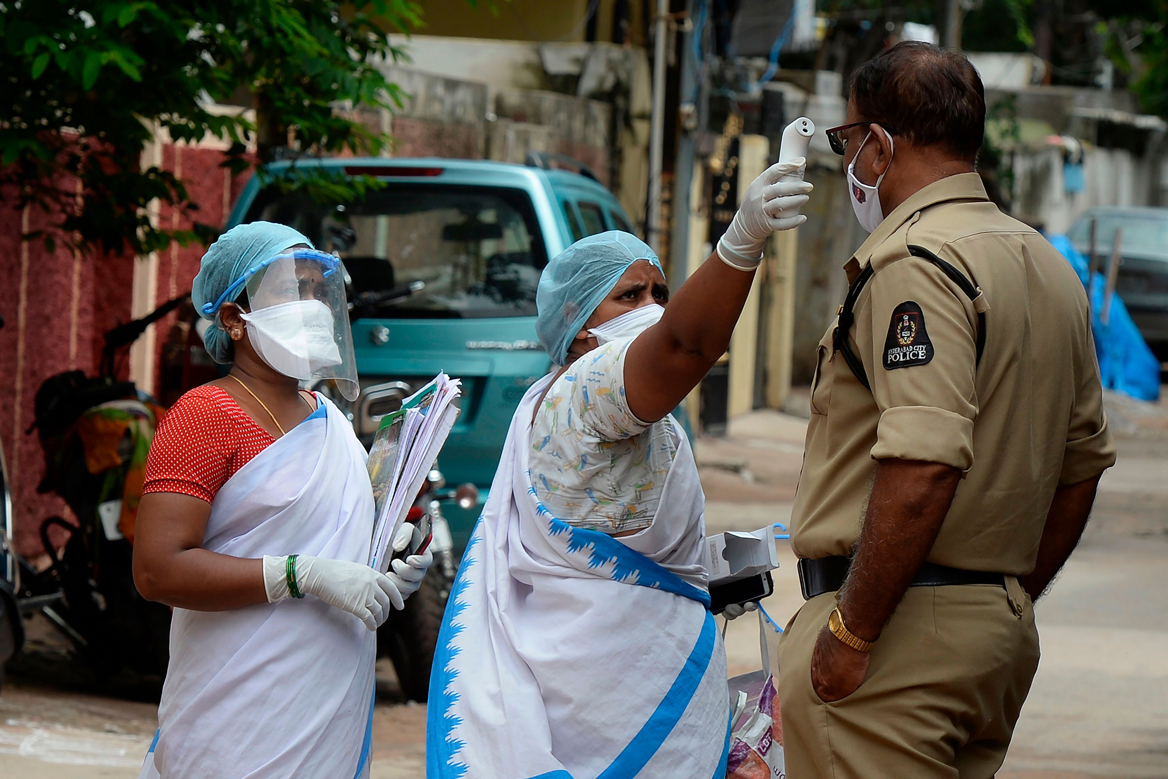 An Accredited Social Health Activists (ASHA) worker (C) checks the temperature of a policeman outside a containment zone. Credits: AFP Photo
