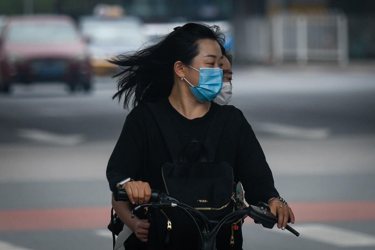 Two women wearing face masks ride an electric sharing bicycle along a street in Beijing on July 3, 2020.  Credit/AFP Photo