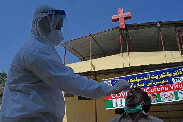 A health official wearing Personal Protective Equipment (PPE) takes a swab sample from a man to test for the Covid-19 coronavirus beside a church during a door-to-door screening and testing operation at a low-income area sealed by the authorities in Islamabad on July 2, 2020, as virus cases continue to rise. Credits: AFP Photo