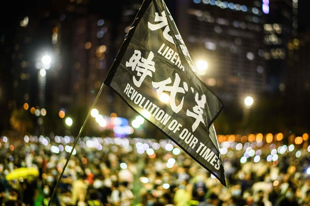 Attendees raise a flag that reads 'Liberate Hong Kong Revolution Of Our Times' during a candlelit remembrance in Victoria Park in Hong Kong on June 4, 2020, after the annual vigil that traditionally takes place in the park to mark the 1989 Tiananmen Square crackdown was banned on public health grounds because of the COVID-19 coronavirus pandemic. Credit/AFP Photo