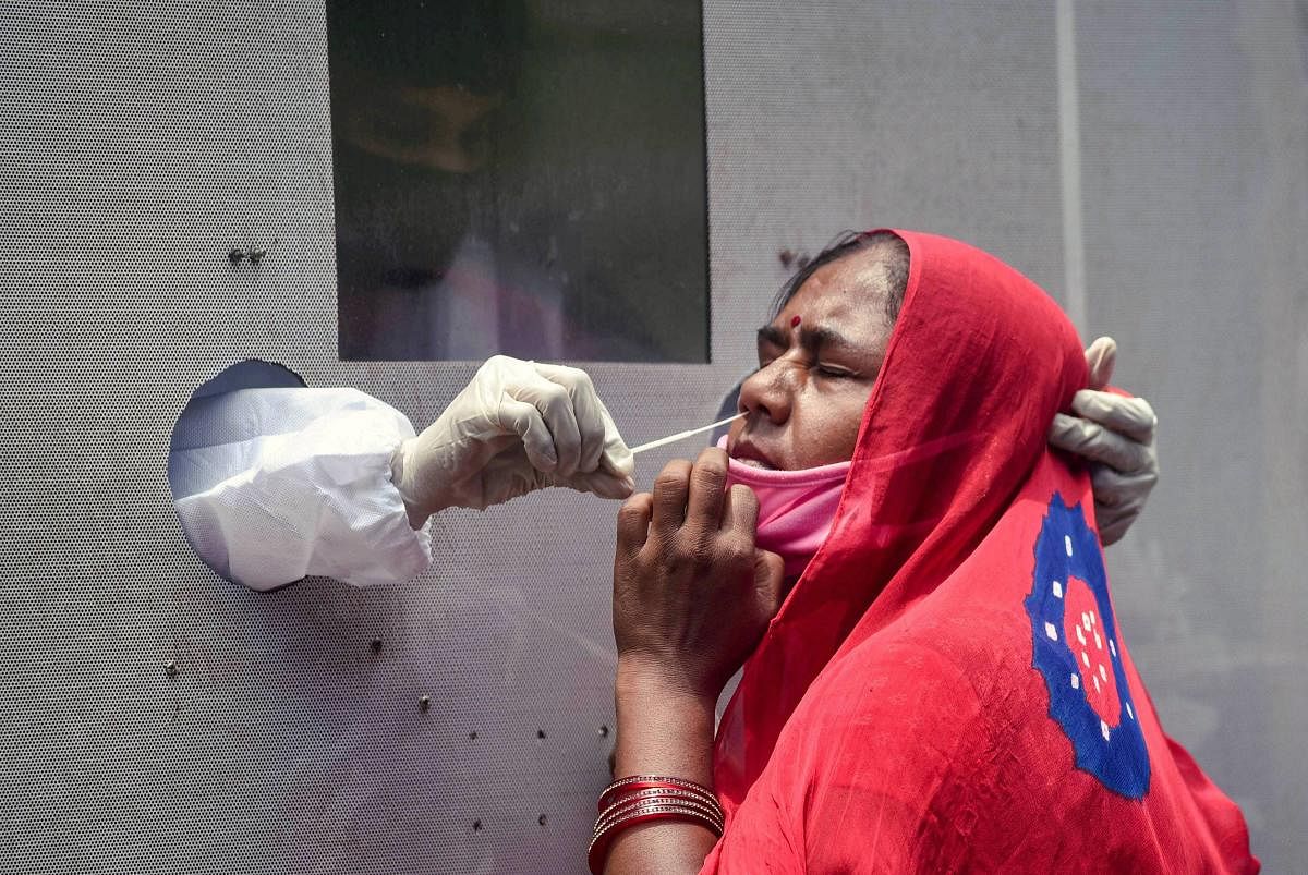 A healthcare worker collects a sample of a woman for the Covid-19 test from a swab collection bus, in Vijayawada. PTI