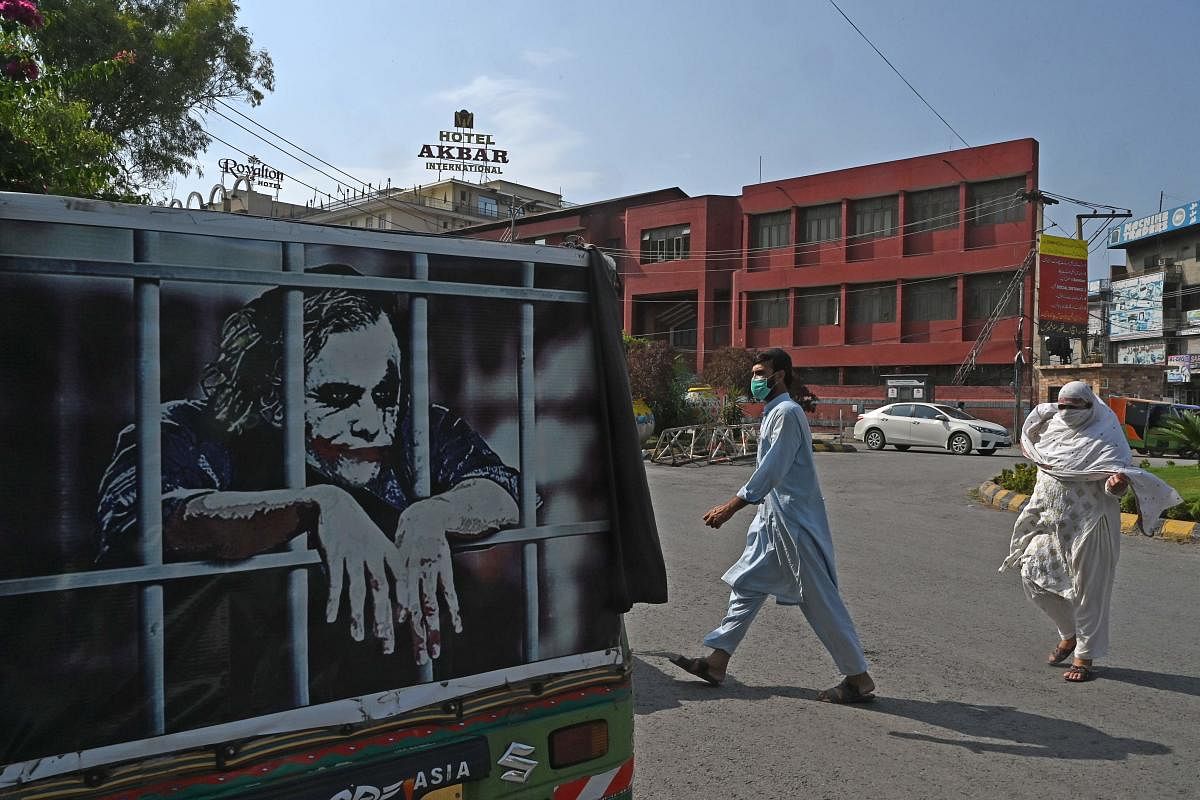 People wearing facemasks cross a street beside an auto-rickshaw with a graffiti depicting actor Heath Ledger (L) in his role as the Joker, in Rawalpindi on June 26, 2020.  Credit/AFP Photo