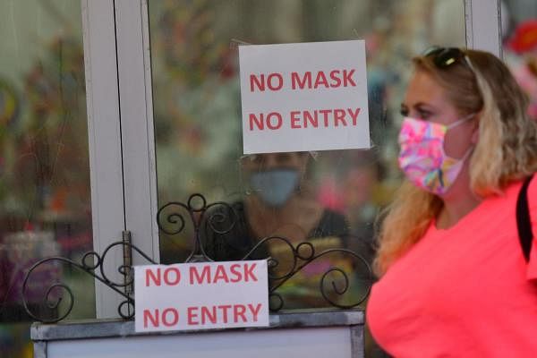 A woman wearing a face mask walks past a Boardwalk store with signs warning patrons of mask requirements on July 3, 2020 in Wildwood, New Jersey. Credits: AFP Photo