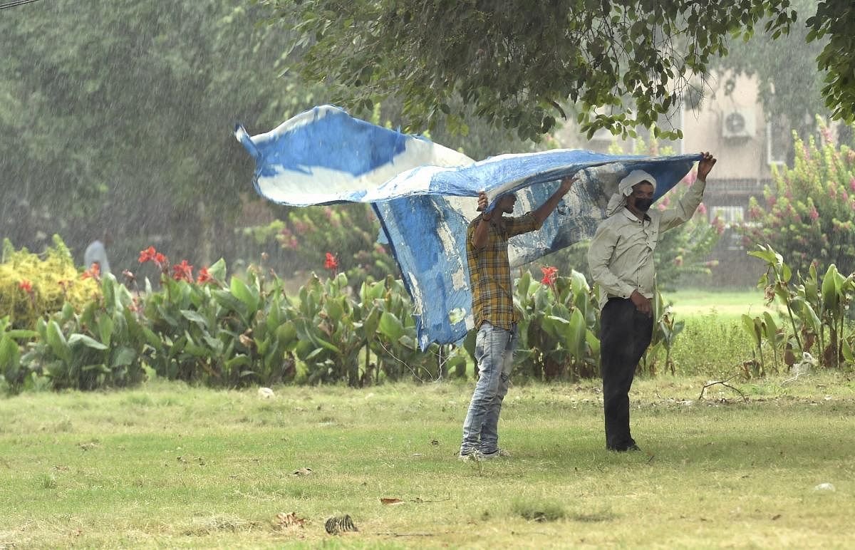 Men cover themselves with a plastic sheet to protect themselves from rain, in New Delhi. PTI