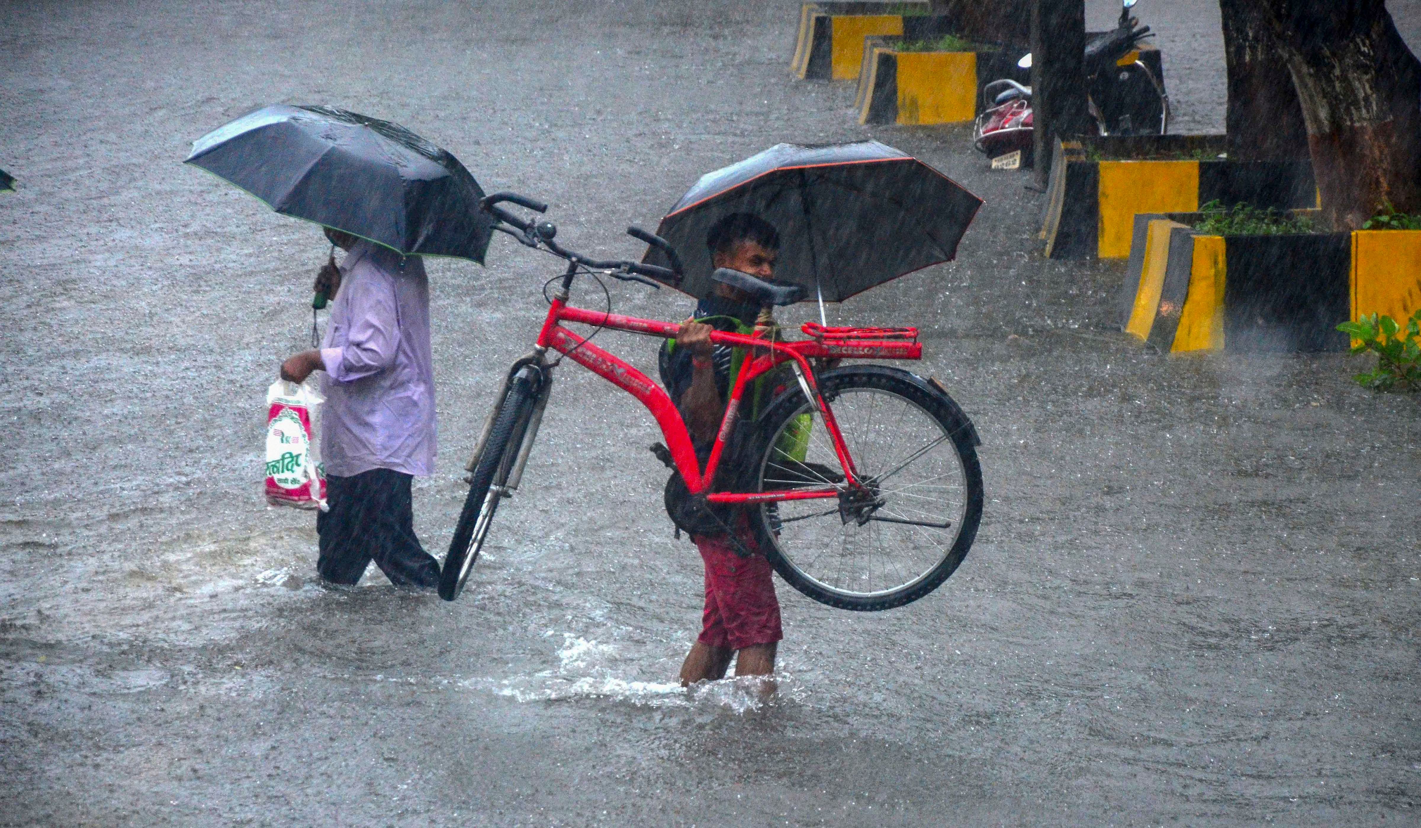 Commuters cross a waterlogged street during heavy rainfall, at Vashi in Navi Mumbai. Credits: PTI Photo
