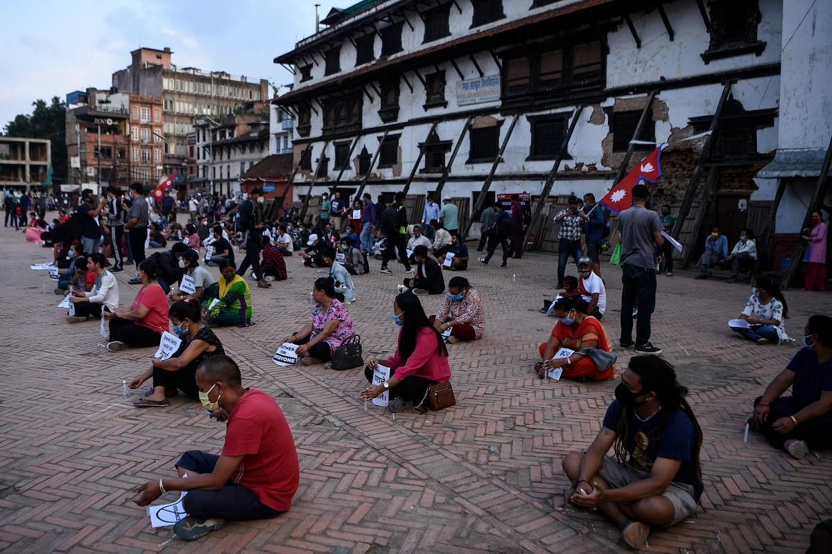 Protesters sit maintaining social distance while holding placards and lit candles during a demonstration against the government's approach on the fight against the COVID-19 coronavirus, in Kathmandu (AFP Photo)