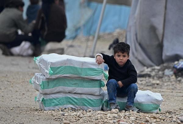 A displaced Syrian boy sits next to humanitarian aid, consisting of heating material and drinking water. Credit: AFP