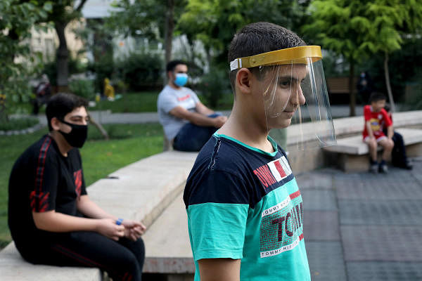 A boy wearing a face shield watches kids playing, following the outbreak of the coronavirus disease (Covid-19), in Tehran, Iran, July 8, 2020. Credit: Reuters Photo