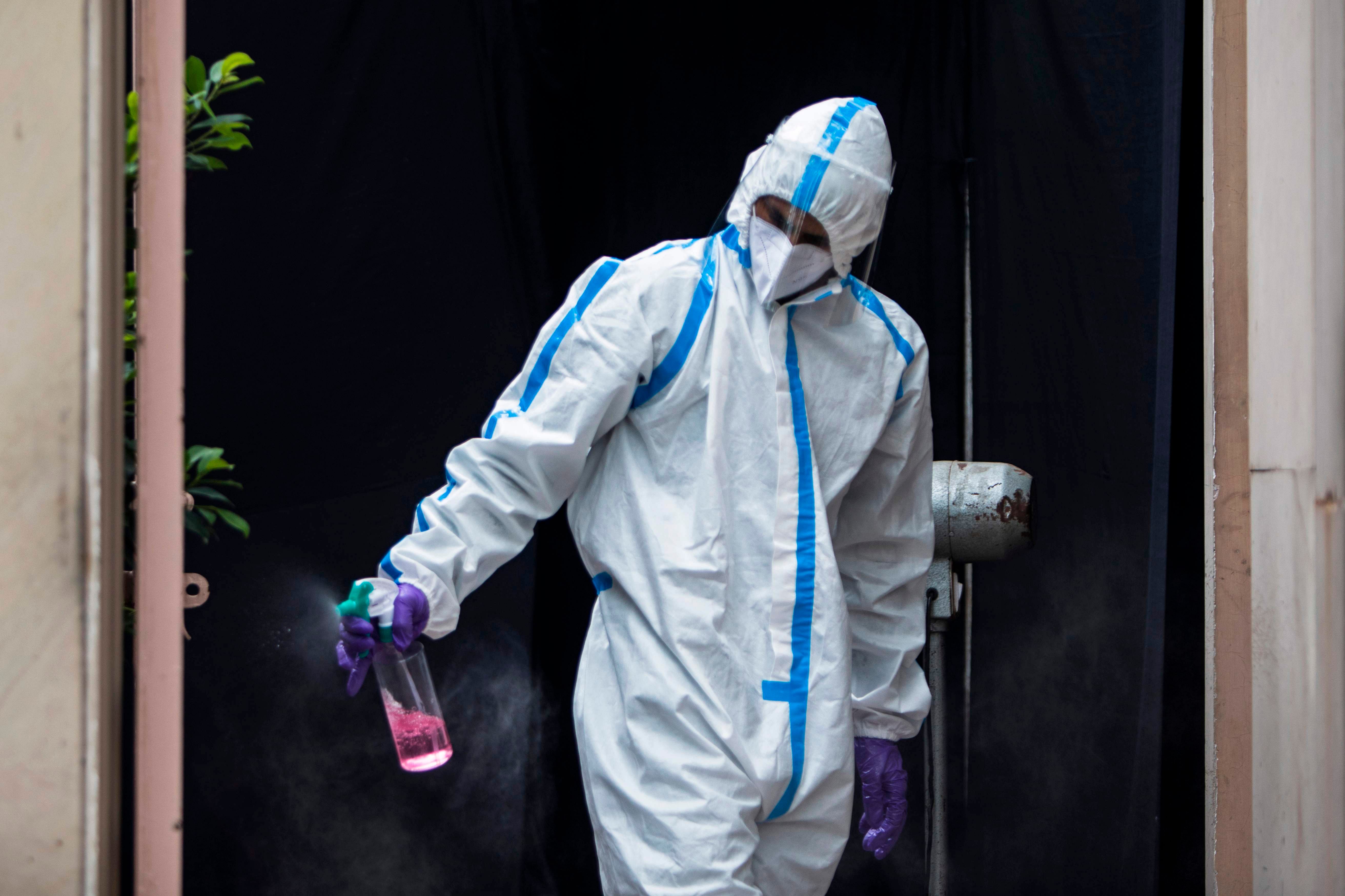 A health official wearing a Personal Protective Equipment (PPE) suit sprays disinfectant at the entrance of a temporary testing facility in Delhi. Credit: AFP