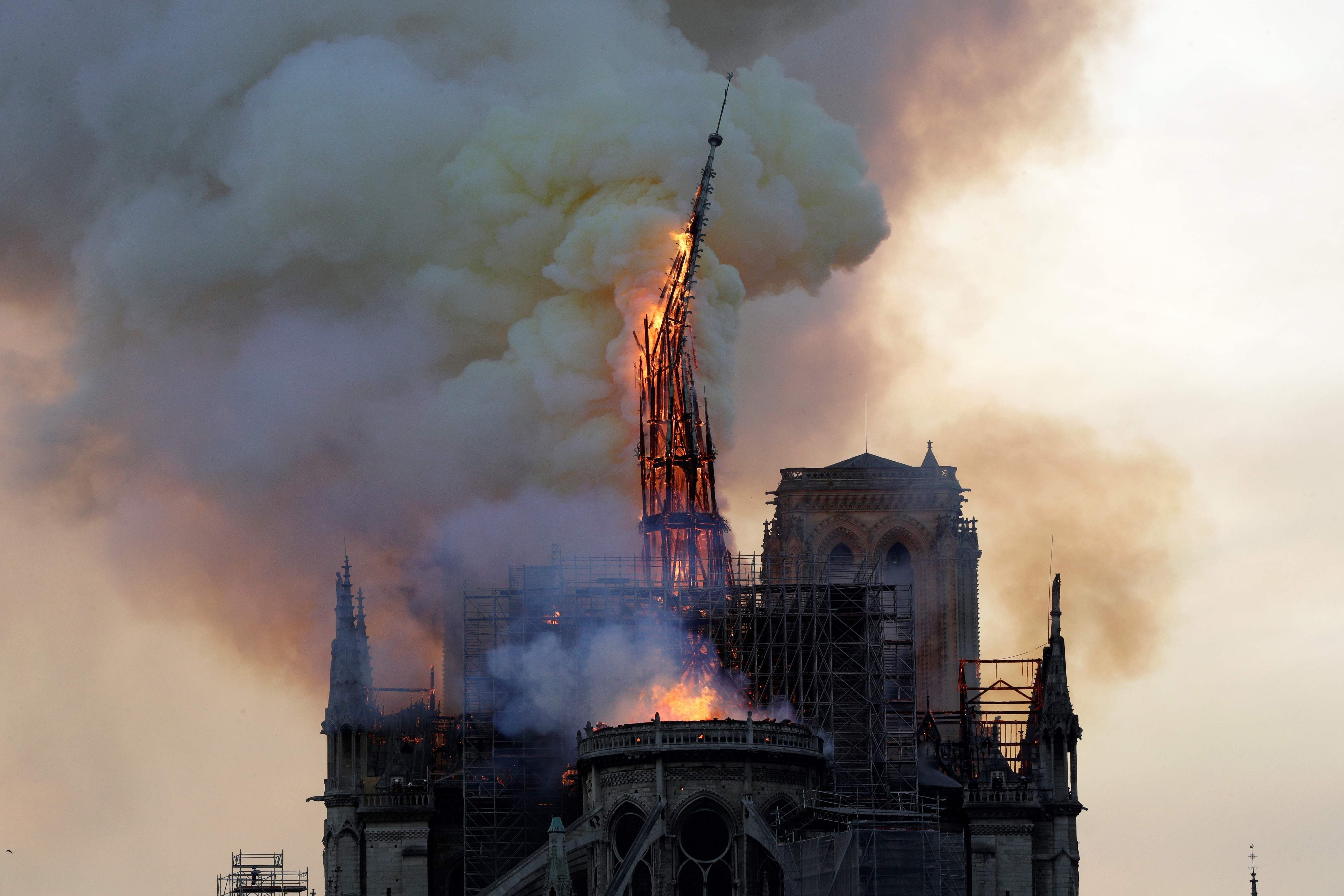 In this file photo taken on April 15, 2019 The steeple and spire of the landmark Notre-Dame Cathedral collapses as the cathedral is engulfed in flames in central Paris. - Emmanuel Macron, who had considered to rebuild Notre-Dame with a new contemporary spire after the blaze, is now coonvinced that the cathedral and its spire must be restored as they were. (Photo by AFP)