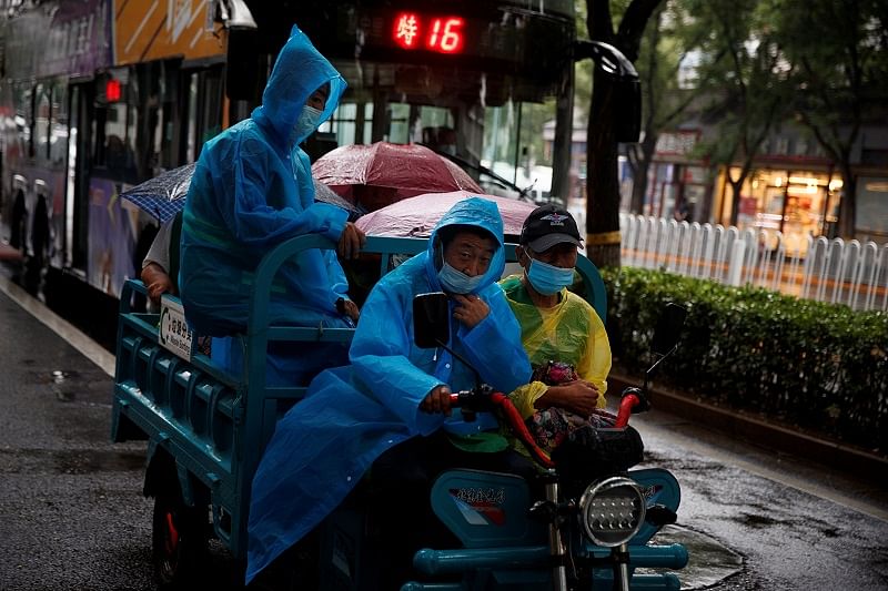 Workers wear protective masks and rain coats as they ride on an electric tricycle on a rainy day following an outbreak of the coronavirus. Credits: Reuters Photo