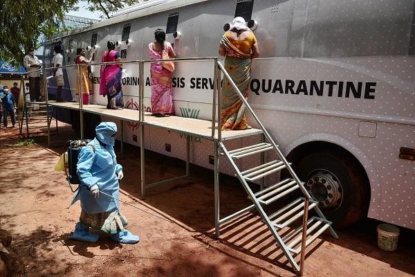 A worker sanitses an area as people wait to undergo Covid-19 tests at a mobile swab collection bus, in Vijayawada, Tuesday, June 23, 2020. Credit: PTI Photo