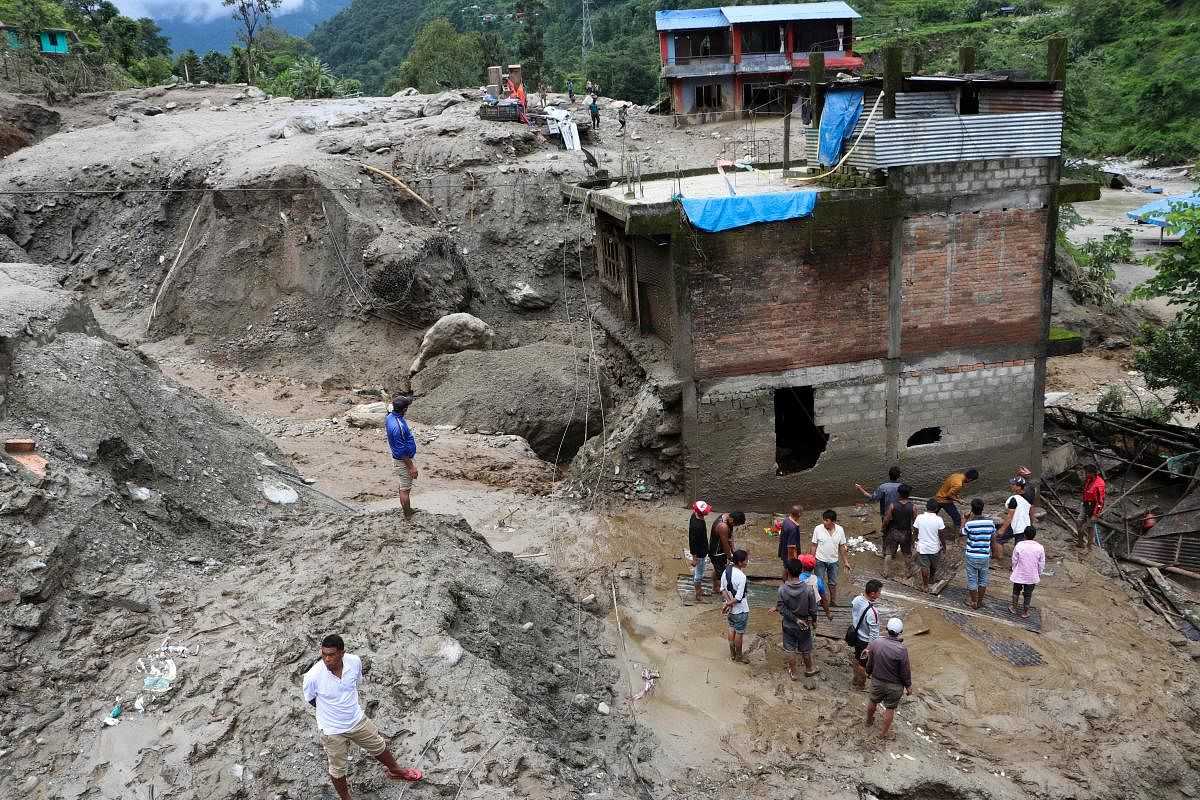 Residents and rescue workers inspect the area outside a house damaged by a landslide and the swell of the Thado-Koshi river due to heavy rains in Jambu village of Sindhupalchok district, some 80 kms northeast of Kathmandu on July 9, 2020. Credit: AFP
