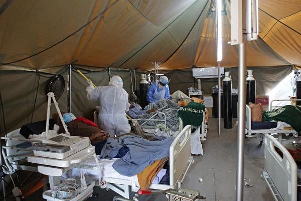 A professional healthcare worker wearing personal protective equipment (PPE) treats a patient in a tent dedicated to the treatment of possible coronavirus patients, while another cleans the ward at the Tshwane District Hospital in Pretoria on July 10, 2020. Credit: AFP Photo